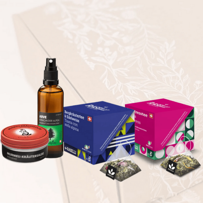 Murmeli Kräutersalbe, Arve Raumduft und Kissenspray, Bio Raselli Bergkräutertee & Edelweiss und Bio Raselli Antistress Tee vor einem transparenten Geschenkbox Nature.