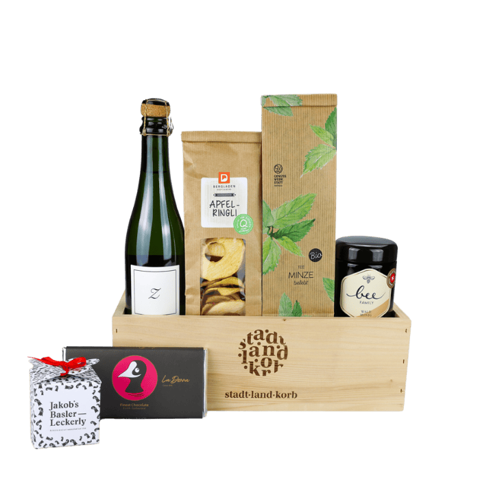Gaumenfreude Geschenkkorb Stadt Land Korb vor weissem Hintergrund befüllt mit Zürischümli, Apfelringli, Minztee, BeeFamily Honig, Taucherli Schokolade und Jakob's Basler Leckerly