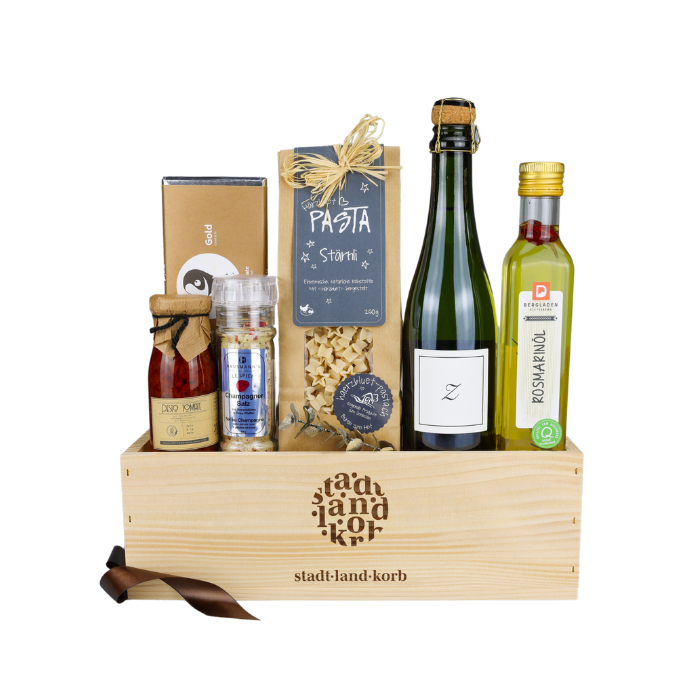 Genuss Oase Geschenkkorb vor weissem Hintergrund befüllt mit Tomatenpesto, Champagner Salz, Stärnli Pasta, Taucherli Gold Schokolade, Zürischum und Rosmarinöl