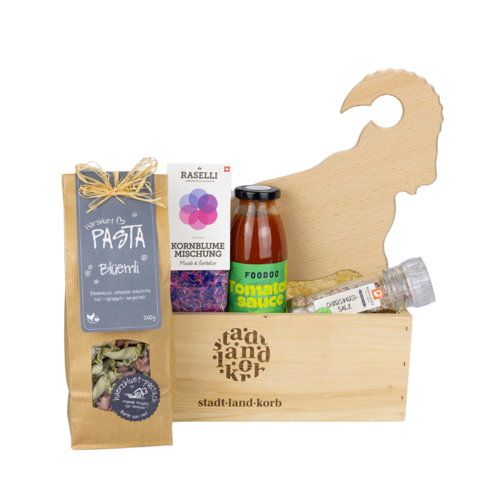 Genussvolle Freuden Geschenkkorb vor weissem Hintergrund befüllt mit Blüemli Pasta, Kornblume Mischung, Foodo Tomatensauce, Chrüsimüsi Salz und Apérobrett Steinbock