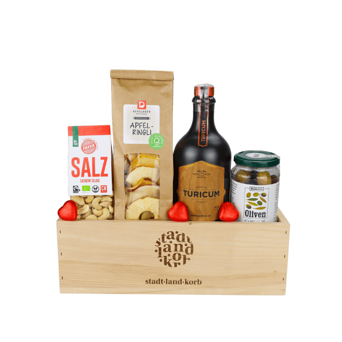 Gin & Genuss Geschenkkorb vor weissem Hintergrund befüllt mit Salz Cashews, Apfelringli, Turicum Wood Bareled Gin, Oliven und Lindt Herzen