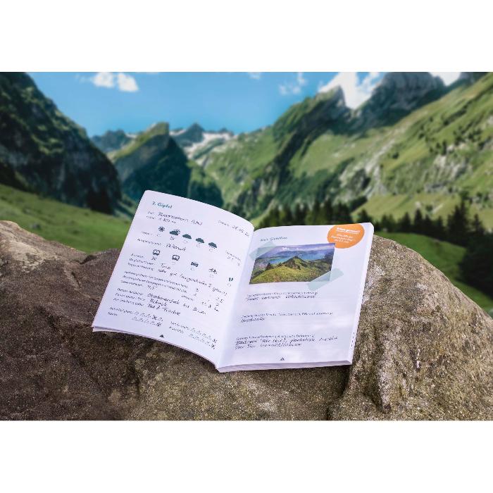 Gipfelbuch auf einem Felsen mit einer Wanderlandschaft im Hintergrund.