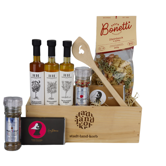 Goldstück Geschenkkorb vor weissem Hintergrund befüllt mit Pepe Ticino, Taucherli Schokolade, Haldihof Essig, Kochlöffel Steinbock, Steinbock Pasta, Champagner Salz und Taucherli Schokolade