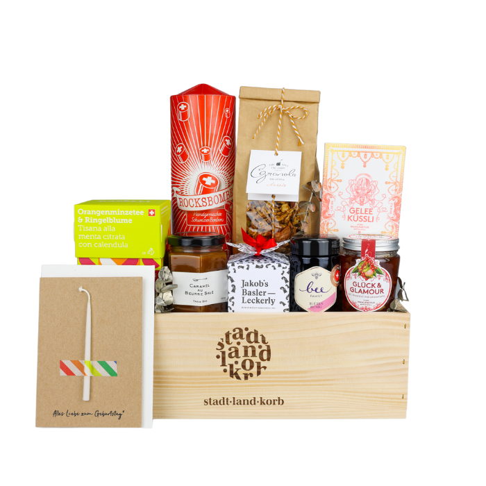 Happy Birthday Geschenkkorb vor weissem Hintergund befüllt mit Bio Raselli Tee, Jakob's Basler Leckerly, Bee Family Honig, Konfitüre, Gelée Küsseli, Tiny Factory Grandola und Rocksbombe