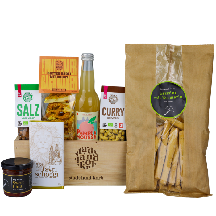 Herzhafter Genuss Geschenkkorb vor weissem Hintergrund befüllt mit Mandeln, Sweet Chili Dip, Tsüri Schokolade, Limonade, Curry Cashews und Grissini