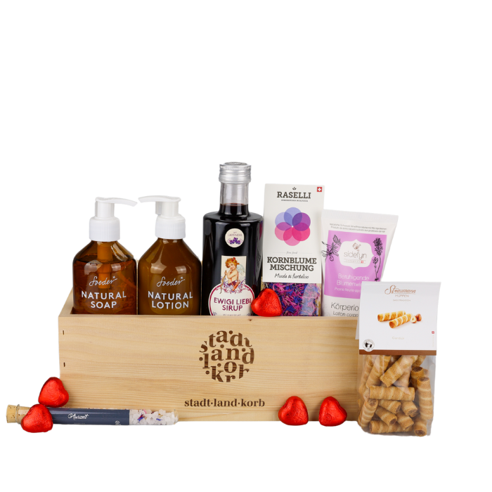 Liebe in einer Box Geschenkkorb vor weissem Hintergrund befüllt mit Soeder Natural Soap, Soeder Natural Lotion, Ewigi Liebi Sirup, Kornblumen, Sidefyn Körperlotion, Straumann Hüppen, Badesalz und Lindt Herzen