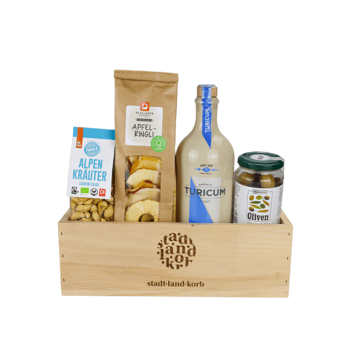 London Dry Genuss Geschenkkorb vor weissem Hintergrund befüllt mit Alpenkräuter Cashews, Apfelringli, Turicum London Dry Gin und Oliven
