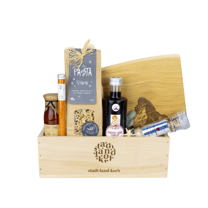 Love is in the air Geschenkkorb vor weissem Hintergrund befüllt mit Stärnli Pasta, Chili Salz, Tomatenpesto, Ewigi Liebi Sirup, Matterhorn Schneidebrett, Champagner Salz