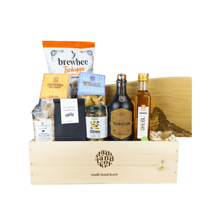 Männer Genuss Geschenkkorb vor weissem Hintergrund befüllt mit Tschipps, Risotto, Pekannüsse, Oliven, Turicum Wood Bareled Gin, Flûtes, Chiliöl, Matterhorn Schneidebrett