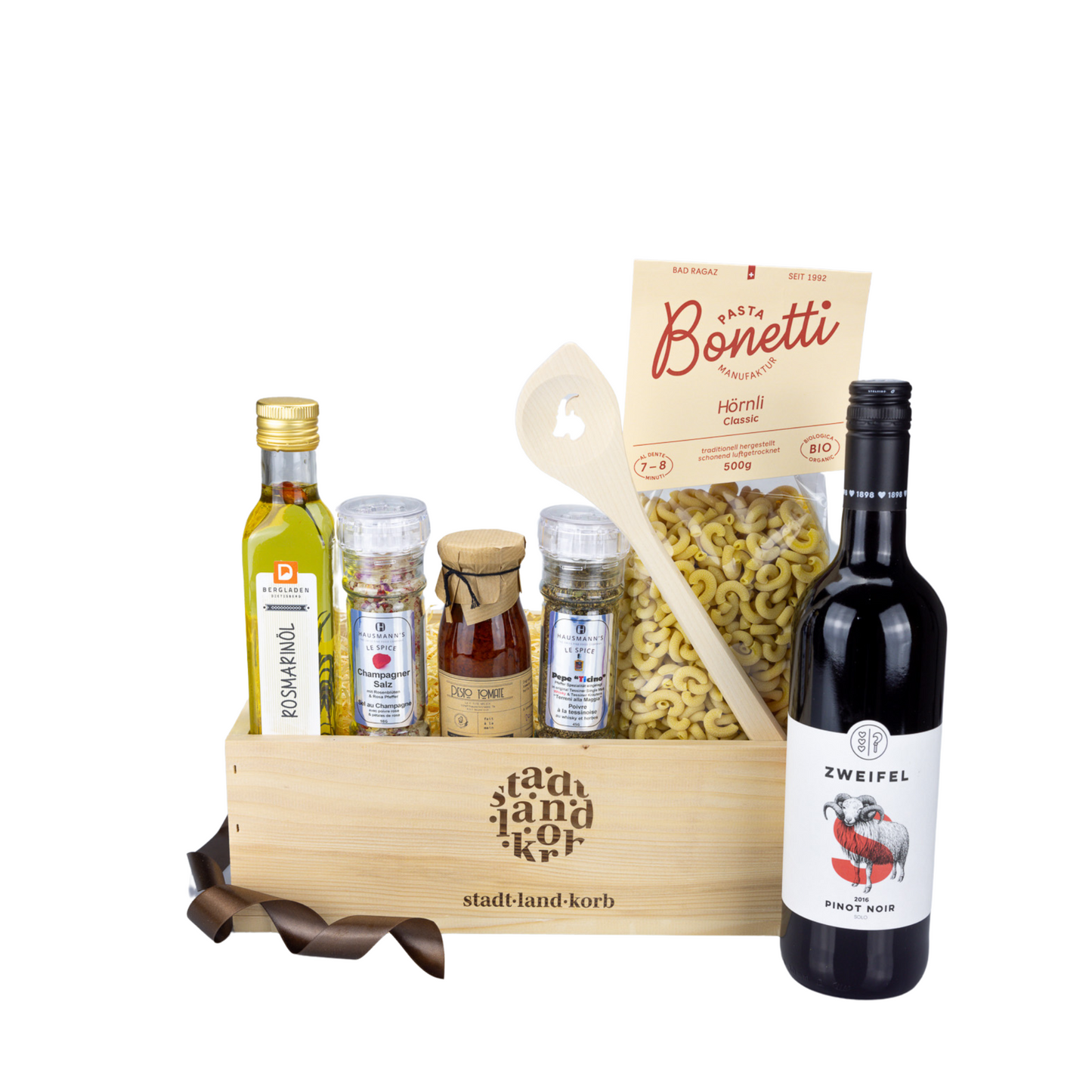 Pinot Noir Dinner Geschenkkorb befüllt mit Rosmarinöl, Champagner Salz, Tomatenpesto, Ticino Pfeffer, Bonetti Pasta, Kochlöffel Steinbock und Zweifelwein vor weissem Hintergrund.
