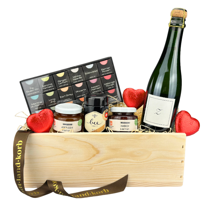 Stadt Land Korb Romantisches Frühstück Geschenkkorb befüllt mit Lindt Schokoherzen, Tee Geschenkschachtel von Länggass Tee, zwei Saisonale Konfitüren, Honig von der Bee Family und einem Zürischun. Vor weissem Hintergrund.