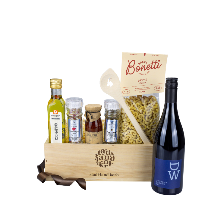 Stadt Land Korb Rotwein Dinner Geschenkkorb befüllt mit Rosmarinöl, Champagner Salz, Tomatenpesto, Pepe Ticini Pfeffer, Bonetti Hörnli, Kochlöffel Steinbock und DW Rotwein vor weissem Hintergrund.