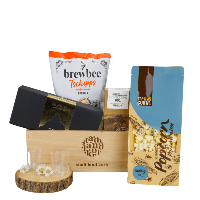 Schnaps & Stil Geschenkkorb vor weissem Hintergrund befüllt mit Alpinte Matterhorn Schnapsgläser, Wanderwasser Schnaps, Brewbee paprika Tschipps, Popcorn