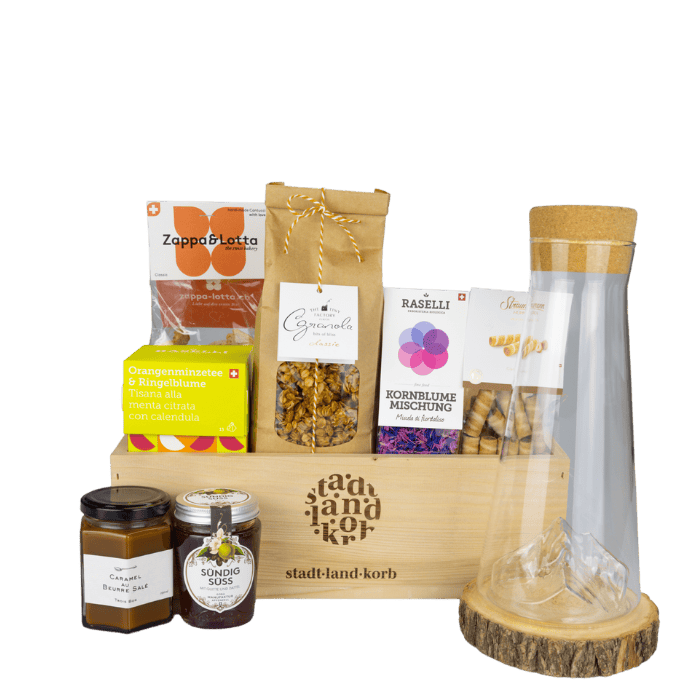 Sonnige Morgenschätze Geschenkkorb vor weissem Hintergrund befüllt mit Honig, Konfitüre, Straumann Hüppen, Tee, Granola und Matterhorn Karaffe
