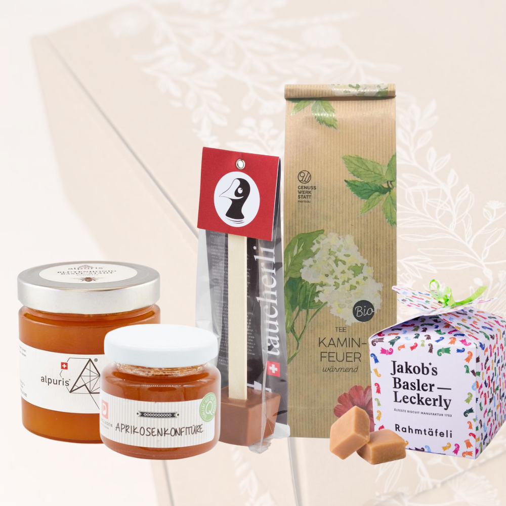 Alpuris Honig, Aprikosenkonfitüre, Taucherli Heissi Schoggi, Kaminfeuer Teeund Jakob's Basler Leckerly vor einer transparenten Stadt Land Korb Nature Geschenkbox.