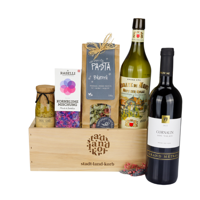 Vino Elegante Geschenkkorb vor weissem Hintergrund befüllt mit Olivenpesto, Kornblumen, Blüemli Pasta, Abbaye e monte und Cornalin Wein