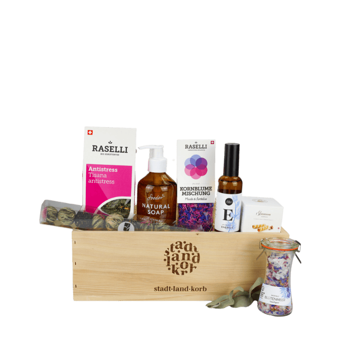 Wohlfühlglück Geschenkkorb vor weissem Hintergrund befüllt mit Bio Raselli Antistress Tee, Teekugeln, Soeder Natural Soap, Kornblumenmischung, Energie Spray, Straumann Hüppen und Badesalz