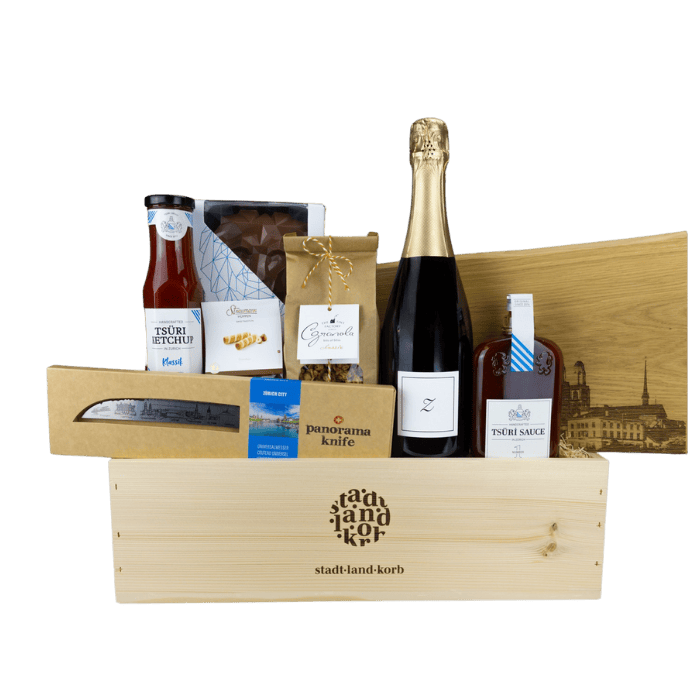 Zürich Deluxe Geschenkkorb vor weissem Hintergrund befüllt mit Zürischum, Tsüri Ketchup, Straumann Hüppen, Granola, Tsüri Sauce, Zürich Schneidebrett, Tsüri Leu, Panoramaknife Zürich