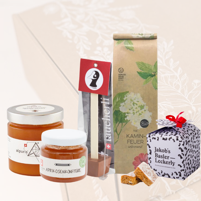 Alpuris Honig, Aprikosenkonfitüre, Taucherli Heissi Schoggi, Kaminfeuertee und Jakob's Basler Leckerly vor einer transparenten Nature Geschenkbox.