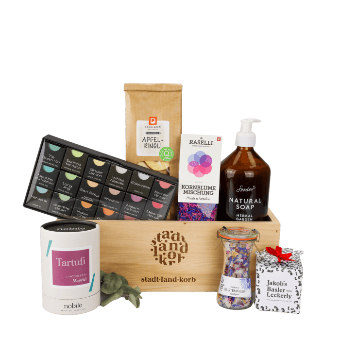 Zuckersüsse Auszeit Geschenkkorb vor weissem Hintergrund befüllt mit Tartufi, Geschenkteeschachtel, Apfelringli, Kornblume Mischung, Soeder Natural Soap, Bütenmeer, Jakob's Basler Leckerly
