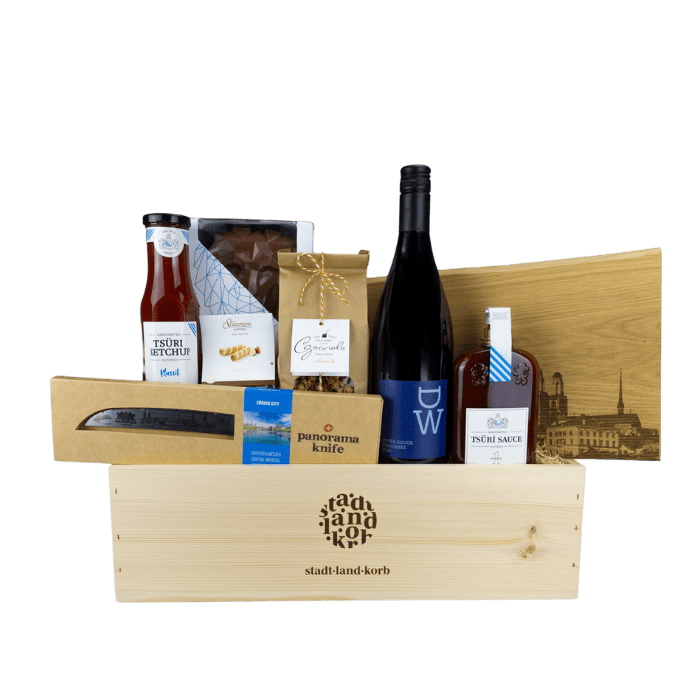 Zürcher Genuss Geschenkkorb vor weissem Hintergrund befüllt mit DW Wein, Tsüri Leu, Straumann Hüppen, Tsüri Ketchup, Zürich Panoramaknife, Tsüri sauce, Zürich Schneidebrett
