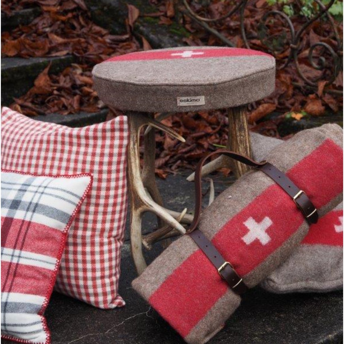 Armeedecke gerollt mit braunem Ledergurt mit MxEskimo Kissen draussen mit Herbstblättern.