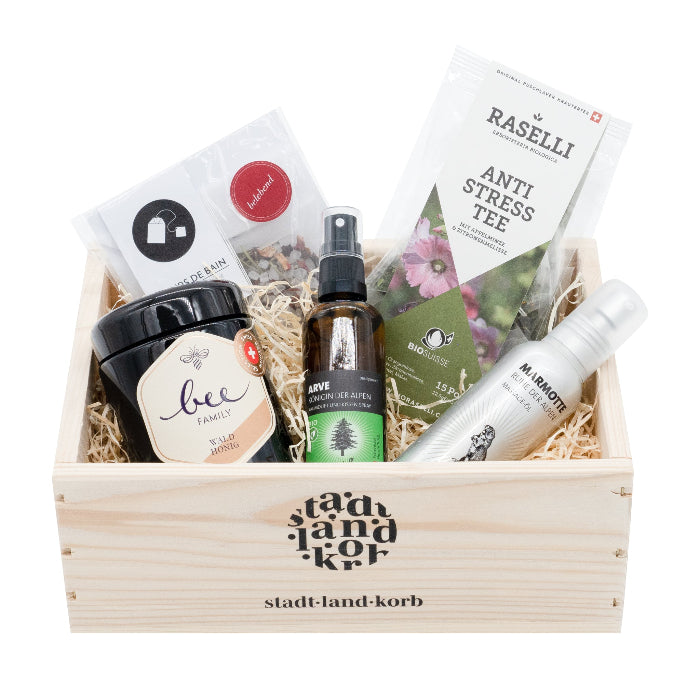 Schau auf Dich Geschenkkorb befüllt mit Waldhonig von der Bee Family, Arve Raumduft & Kissenspray, Marmotte Massageöl, Raselli Antistress Tee und Badesalz vor einem weissen Hintergrund.