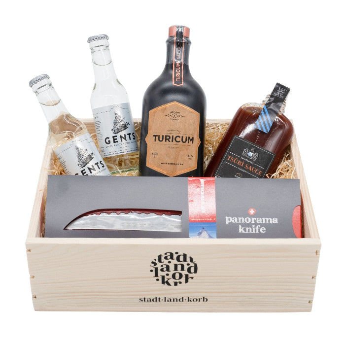 Stadt Land Korb Tsüri Gentleman Geschenkkorb befüllt mit zwei Gents Tonics, Turicum Wood Barreled Gin, Tsüri Sauce und panoramaknife vor weissem Hintergrund.