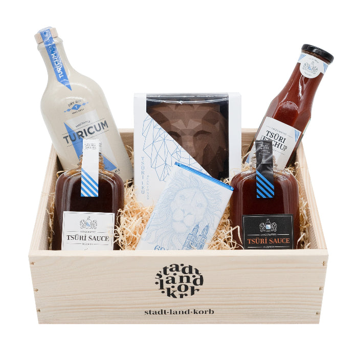 Stadt Land Korb Tsüri Geschenkkorb befüllt mit Turicum Gin, Tsüri Sauce 1 und 3, Tsüri Ketchup, Tsüri Schokolade und Tsüri Leu vor weissem Hintergrund.