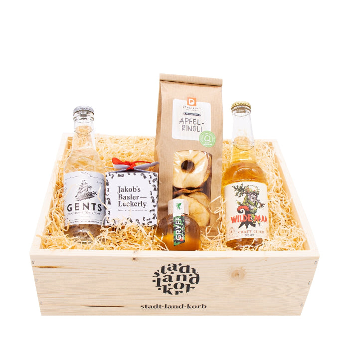 Stadt Land Korb Wilde Maa Geschenkkorb  befüllt mit Gents Tonic, Jakob's Basler Leckerly, Apfelringli, Wilde Maa Cider und Vogel Gryff Spirit vor weissem Hintergrund.