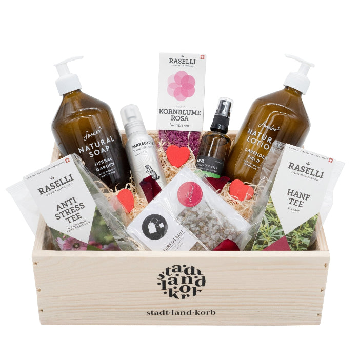 Stadt Land Korb Zeit für Dich Geschenkkorb befüllt mit Bio Raselli Antistress Tee, Hanftee, Soeder Natural Soap, Marmotte Massageöl, Raselli essbare Kornblumen, Badesalz, Arve Raumduft und Soeder Natural Lotion vor weissem Hintergrund.