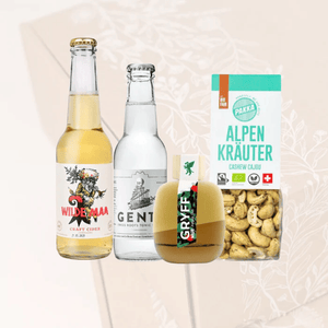 Wilde Maa Craft Cider, Swiss Gents Tonic Water, Gryff Spirits Wilde Apple Gin und Pakka Alpenkräuter Cashews vor einer transparenten Geschenkbox 