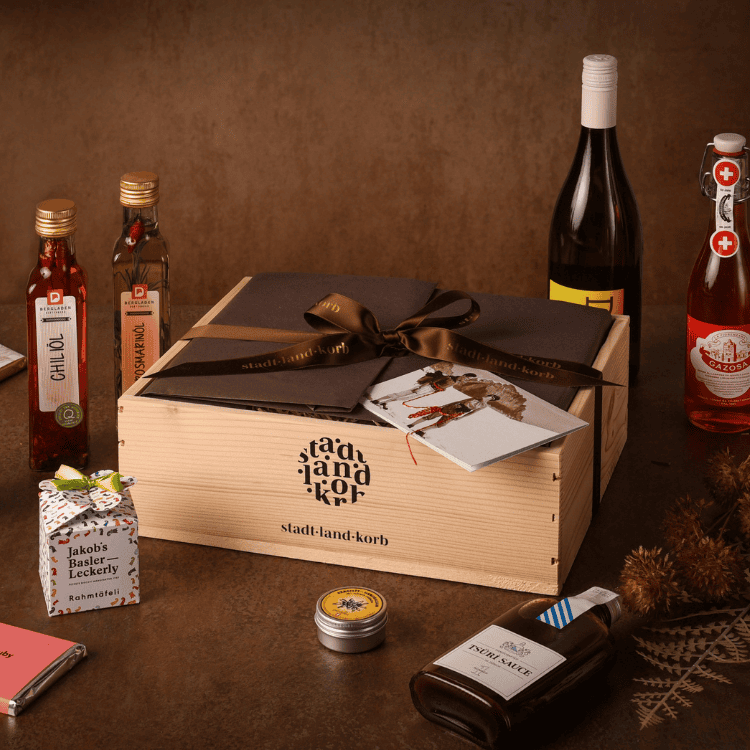 Stadt Land Korb Geschenkkorb mit regionalen Produkten rundherum vor braunem Untergrund.