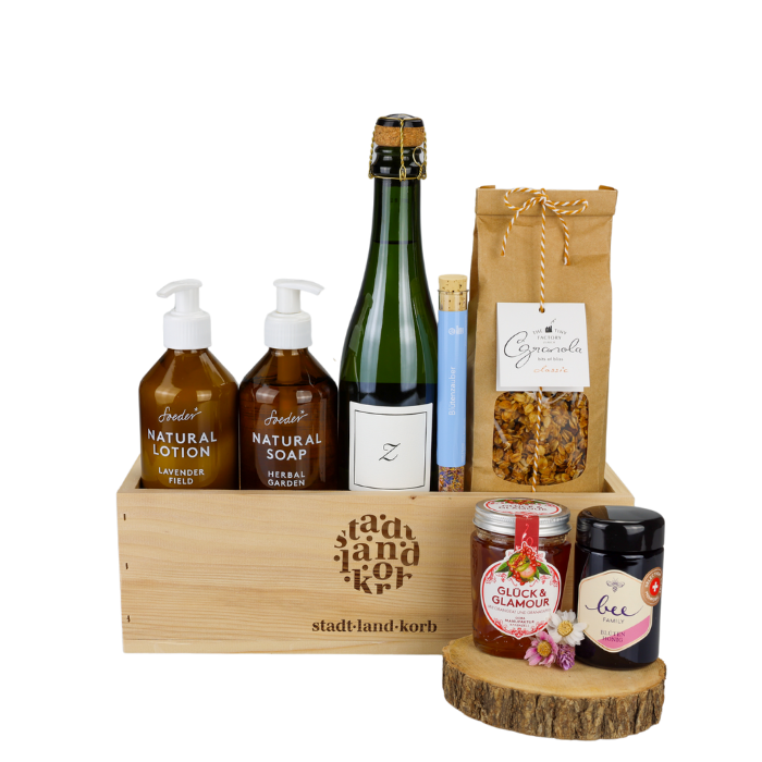 Glanz & Genuss Geschenkkorb vor weissem Hintergrund befüllt mit Soeder Natural Lotion & Natural Soap, Zürischum, Blütenzauber, Granola, Konfitüre und Honig