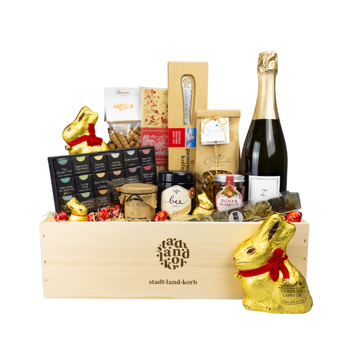 Osterfrühstück Deluxe Geschenkkorb vor weissem Hintergrund befüllt mit Tee Geschenkschachtel, Honig, Konfitüre, Panoramaknife, Teekugeln, Zürischümli, Granola, Straumann Hüppen, weisse Schokolade, Lindt Schokoladenhasen und Schokoladeneier