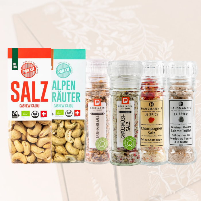 Salzige Sensationen Geschenkbox Nature: PAKKA Salz Cashews, PAKKA Alpenkräuter Cashews, Bärgmannesalz, Chrüsimüsi-Salz, Champagner Salz, Tessiner Merlotsalz vor einer transparenten Nature Box als Hintergrund. 