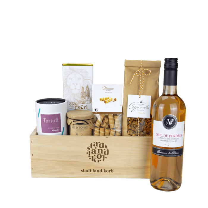 Schöne Genussmomente Geschenkkorb vor weissem Grund befüllt mit Tartufi, Tsüri Schokolade, Gelee de Prosecco, Straumann Hüppen, Granola und Oeil de Perdrix Wein