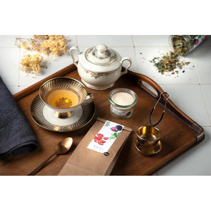 Engelitee im Beutel auf einem Holztablar mit Teekrug, Teetasse, Löffel und Zucker. 